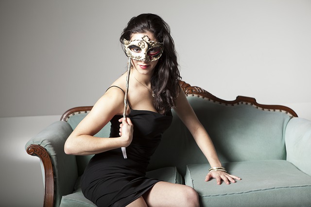 Žena ve společenských šatech držící si pře oči plesovou masku