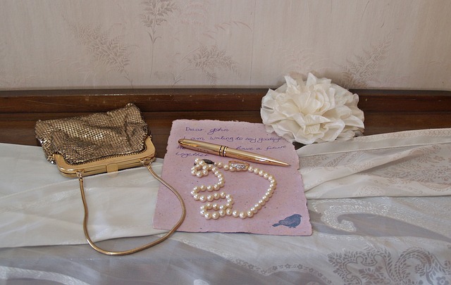 Kovová kabelka-psaníčko, vedle ní položená šňůra perel a dopis